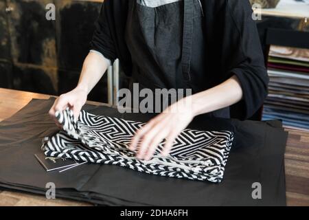 Midsection of young female owner with fabric on wrapping paper at store Stock Photo