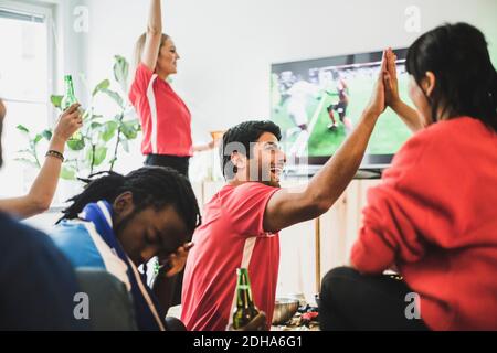 Young man sitting upset while red team celebrating victory at home Stock Photo