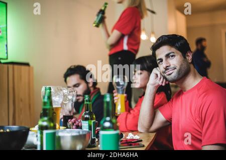 Portrait of young man sitting with friends while watching soccer at home Stock Photo