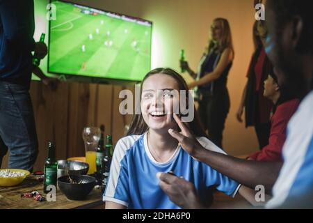 Man applying face paint on woman cheek while watching soccer match at home Stock Photo
