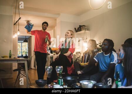 Smiling male and female friends watching soccer match in living room Stock Photo