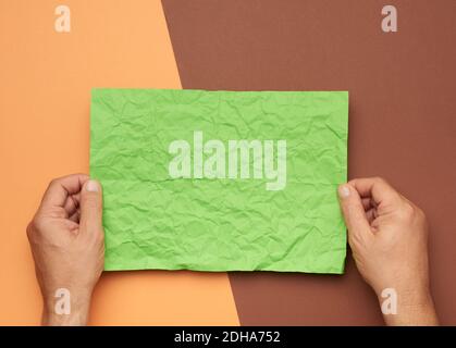 Two male hands are holding blank crumpled green sheet of paper on a brown background Stock Photo