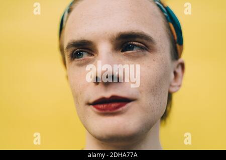Smiling young man looking away while standing against yellow background Stock Photo