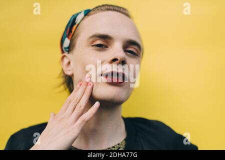 Portrait of smiling man touching cheek while standing against yellow background Stock Photo