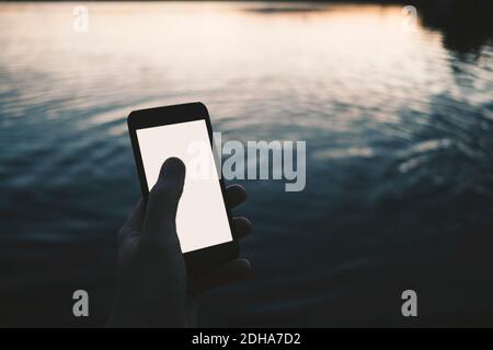 Cropped image of man using smart phone at lake Stock Photo