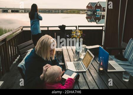 Woman teaching daughter in using digital tablet while friend talking on mobile phone Stock Photo