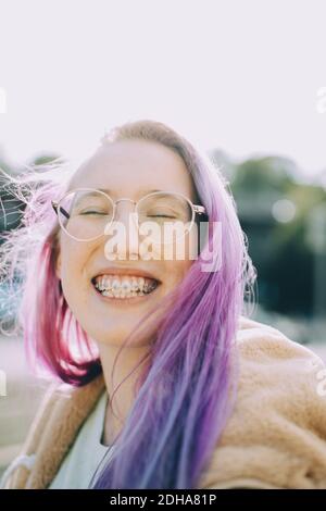 Smiling teenage girl with eyes closed while standing against clear sky Stock Photo