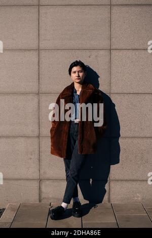 Portrait of contemplating young woman with hands in pockets standing against wall Stock Photo