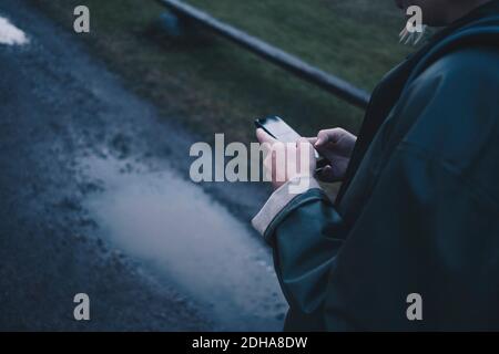 Cropped image of woman using smart phone on wet road Stock Photo