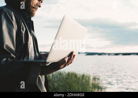 Midsection of man using laptop by lake against sky Stock Photo