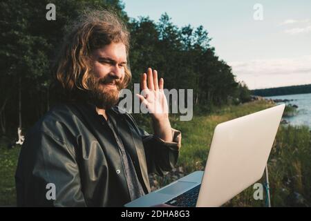 Smiling man doing video call on laptop against forest Stock Photo