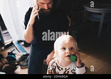 Father talking on mobile phone while girl playing with toy at home Stock Photo