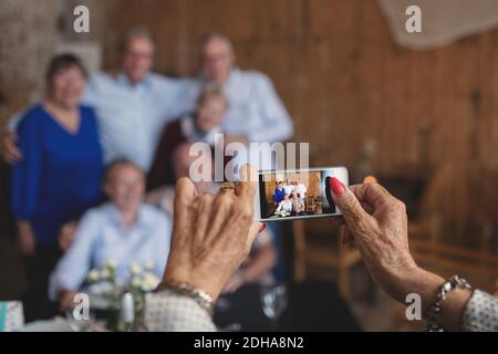 Cropped image of senior woman photographing friends with smart phone at restaurant Stock Photo