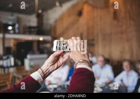 Cropped image of senior woman photographing friends with smart phone at restaurant Stock Photo