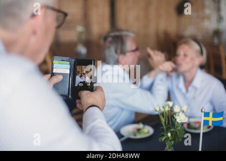 Senior man photographing couple having drinks in restaurant Stock Photo