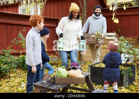 Male and female collecting fresh produce from garden while children standing in yard Stock Photo
