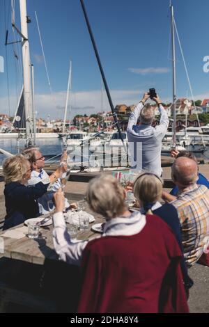 Senior man with friends taking selfie using mobile phone at restaurant patio Stock Photo