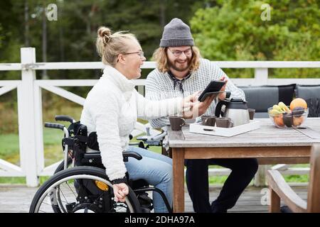 Young male caretaker and disabled woman using digital tablet in yard Stock Photo