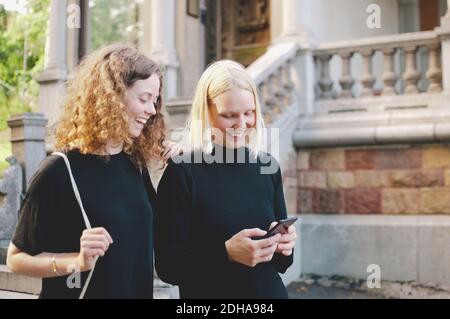 Cheerful young student with female friend using mobile phone by university Stock Photo