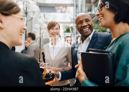 Happy male and female business people talking while standing in office Stock Photo