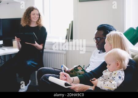 Working mother with baby discussing with colleagues in creative office Stock Photo
