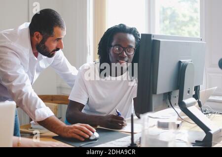 Businessmen discussing while using computer at desk in creative office Stock Photo