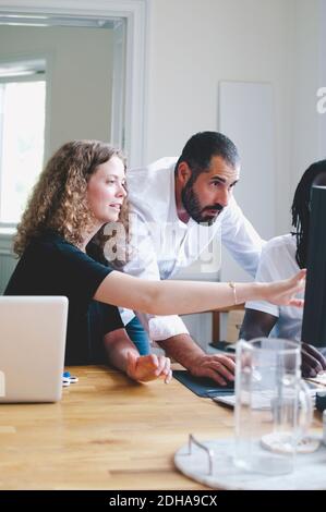 Businesswoman discussing with colleagues over computer in creative office Stock Photo