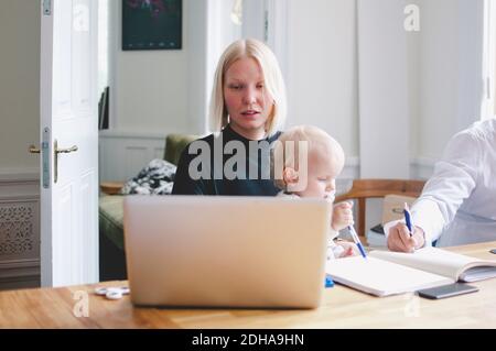 Businesswoman with baby girl using laptop at table in creative office Stock Photo