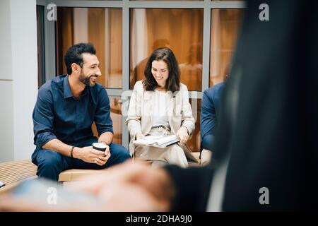 Smiling male and female entrepreneurs talking while sitting against office Stock Photo