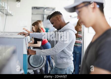 Male and female university students using washing machine at laundromat Stock Photo