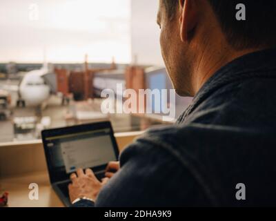 Rear view of mature man using laptop while sitting at airport Stock Photo