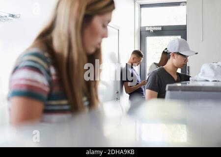 Man using phone while university friends working at laundromat Stock Photo