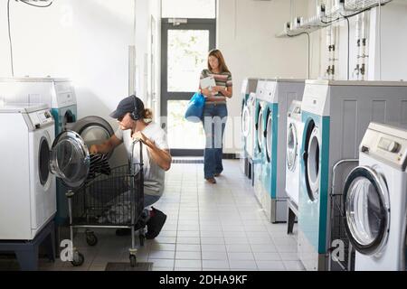 Man using washing machine while woman walking in laundromat Stock Photo