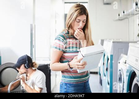 Woman reading information on detergent pack while man using washing machine at laundromat Stock Photo