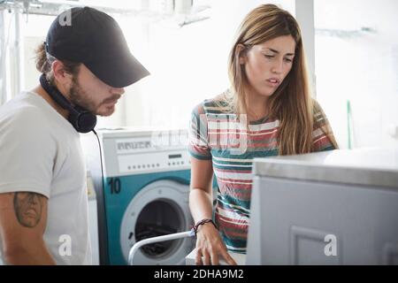 Man assisting female friend in using washing machine at laundromat during sunny day Stock Photo