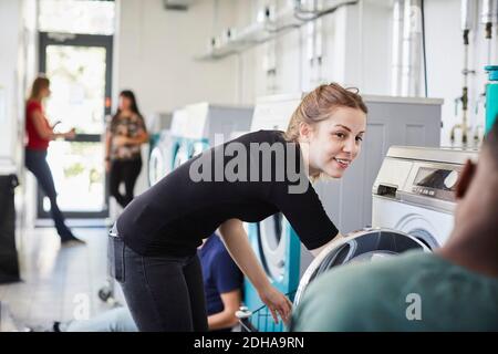 Smiling woman looking at friend while doing laundry Stock Photo