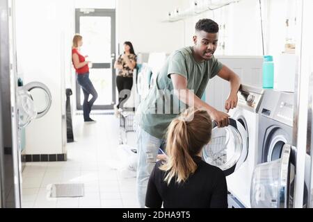 University student talking to woman by washing machine while friends standing in background Stock Photo