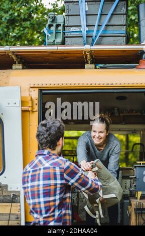 Smiling woman giving luggage to man for unloading from caravan during camping Stock Photo