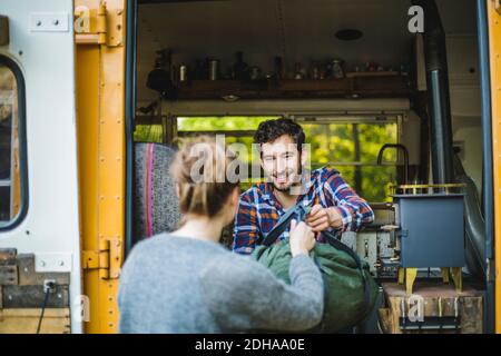 Smiling man giving luggage to woman for unloading from caravan during camping Stock Photo