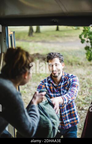 Smiling man taking luggage from woman while unloading caravan during camping Stock Photo