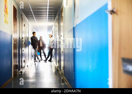 Full length of students talking while standing in corridor at university Stock Photo