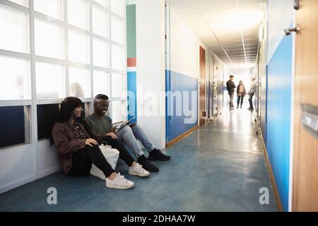Friends using digital tablet while students standing in corridor at university Stock Photo