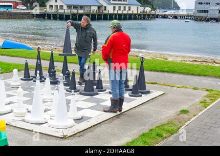 Oban, New Zealand - October 31 2020; Chess players on oversized outdoor board and set on Half Moon Bay waterfront, Stewart Island. Stock Photo