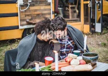 Young multi-ethnic couple wrapped in blanket spending leisure time together during camping Stock Photo