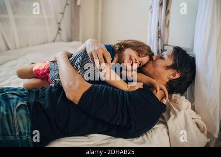 Mature father kissing daughter while lying on bed Stock Photo