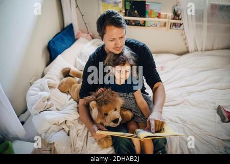 High angle view of father reading book with daughter while sitting in bedroom Stock Photo