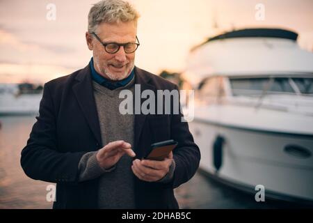 Senior man using smart phone while standing at harbor Stock Photo