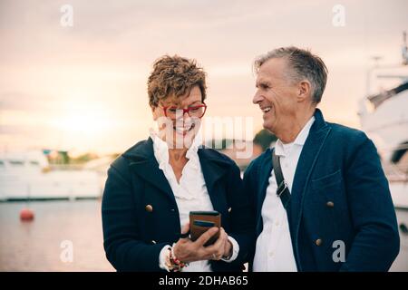 Happy senior woman using smart phone while standing by man at harbor Stock Photo