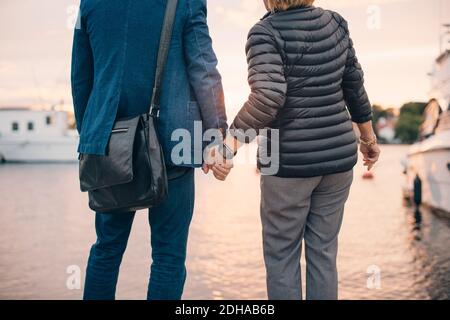 Midsection of senior couple holding hands while standing at harbor Stock Photo