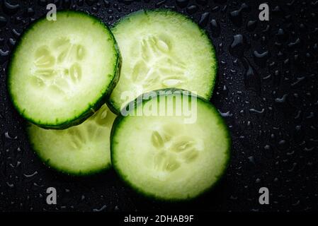 Cucumber slices. Pieces of fresh cucumber on black wet table with water drops. Stock Photo